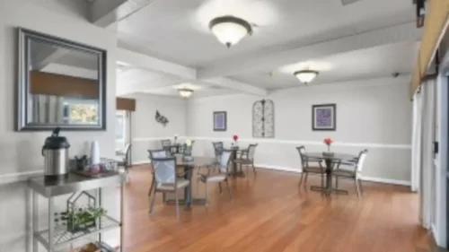 A dining area with a wood floor, several tables and chairs, a mirror on the left, and a fireplace in the back