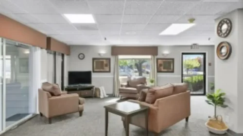 A living room with brown couches, a coffee table, a television, and large windows leading to an outdoor patio
