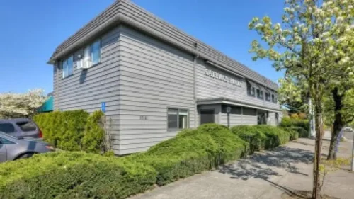 The exterior of a two-story gray building with a sign that reads Waterman House, surrounded by well-manicured hedges